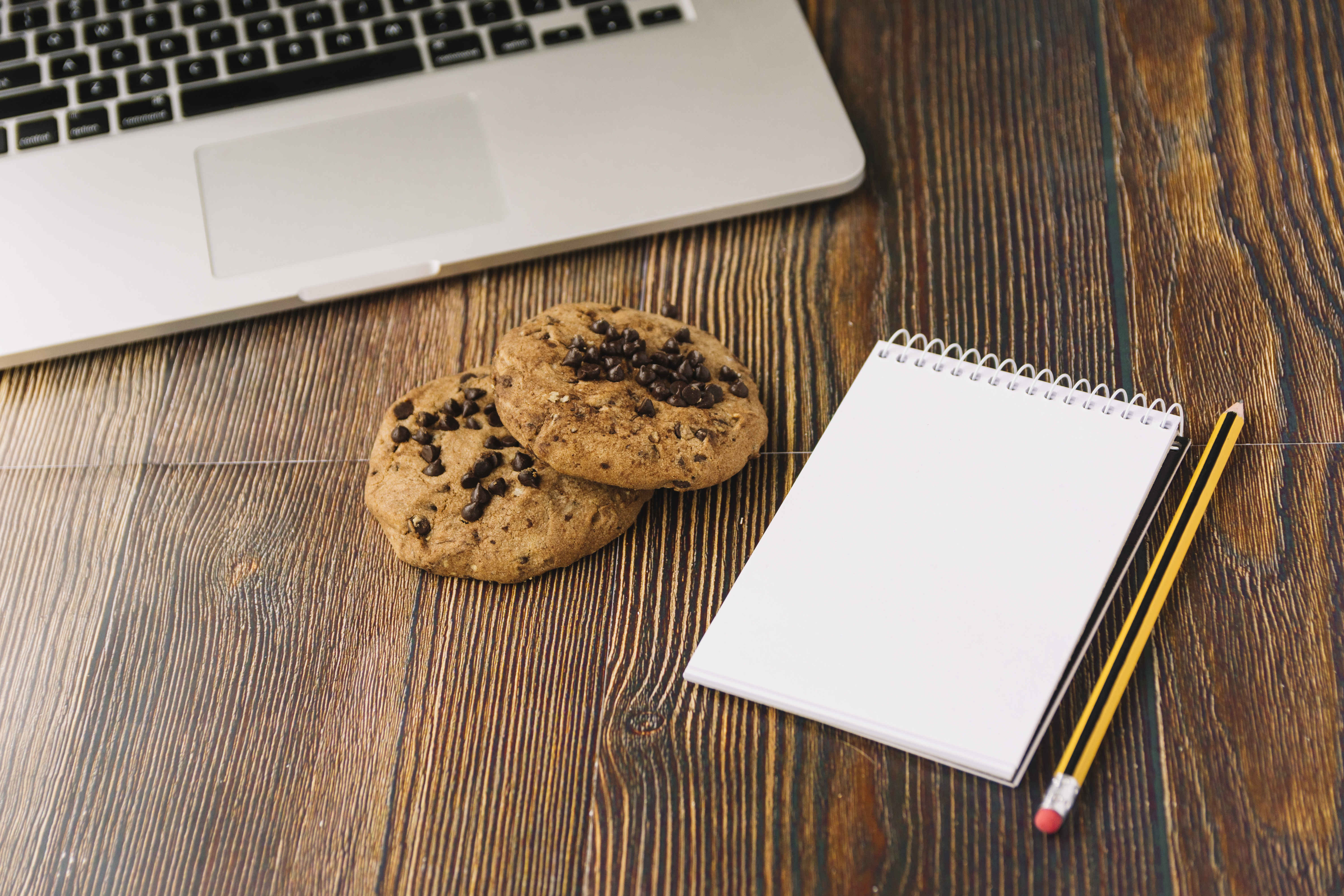 Workspace scene with a laptop, notebook, and nearby biscuits for a snack break.