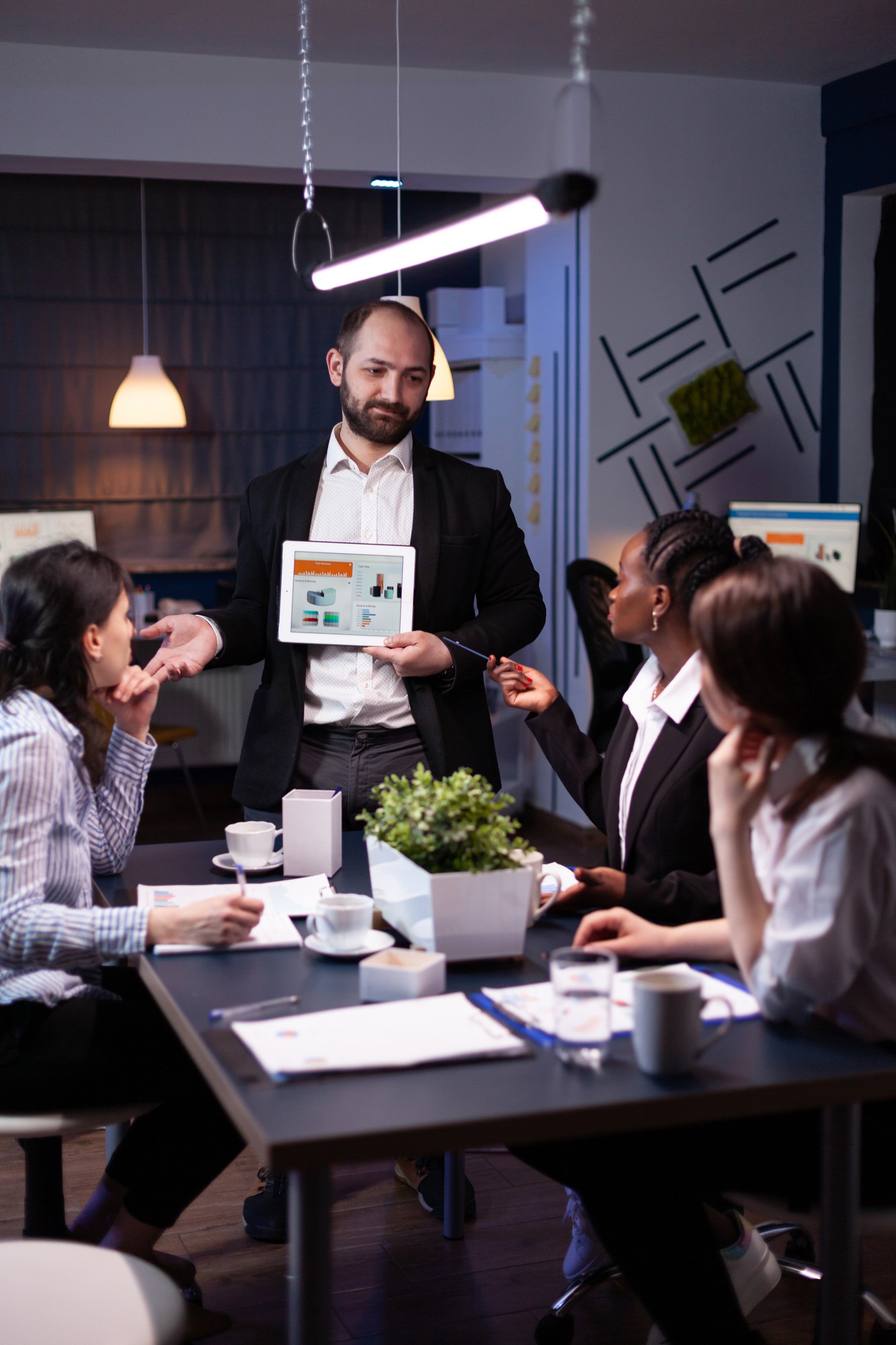 Man standing with an ipad in hand, pitching ideas and discussing business with colleagues in a meeting. 