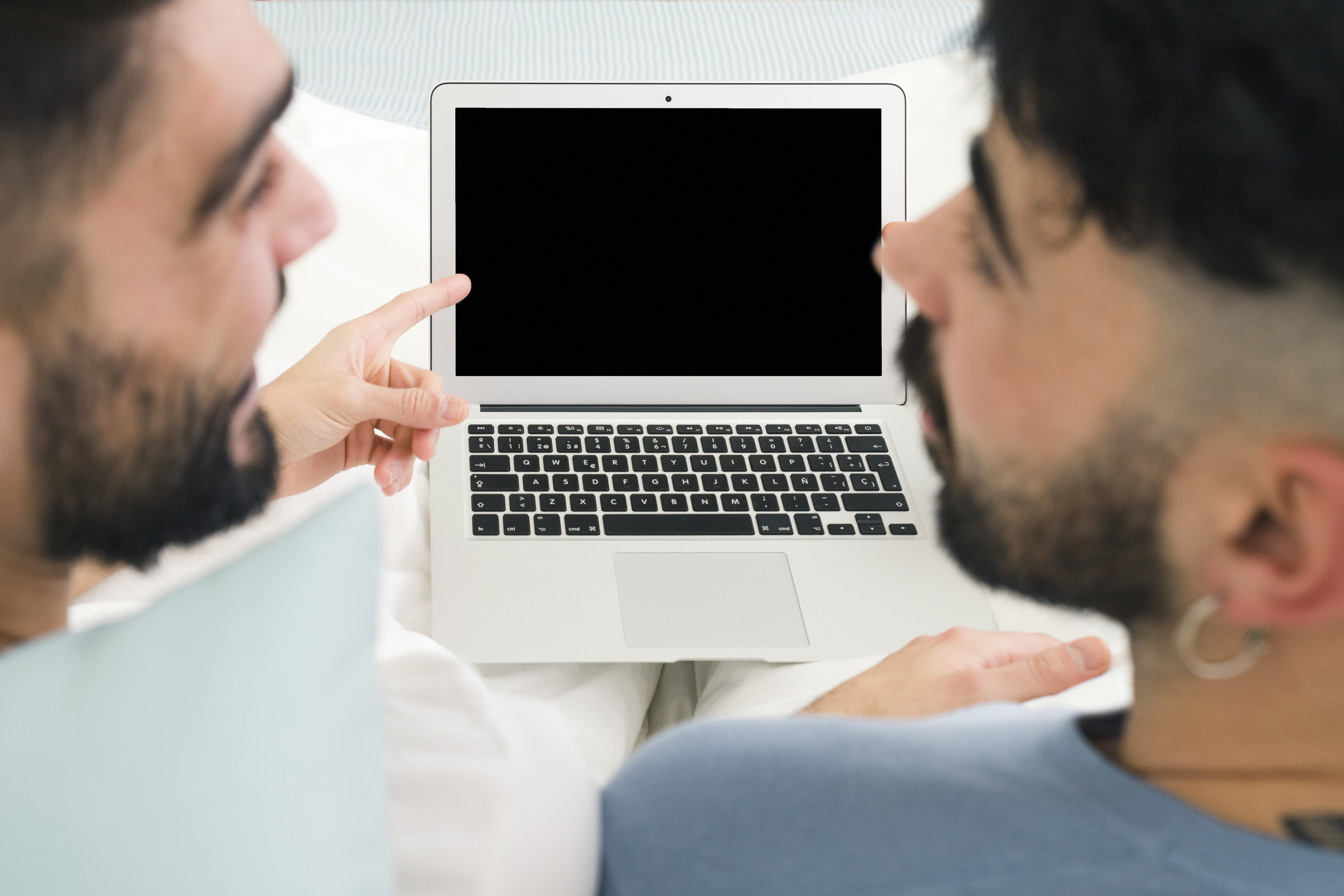 Close-up of a man pointing at something on a laptop screen, possibly showing it to someone off-camera.