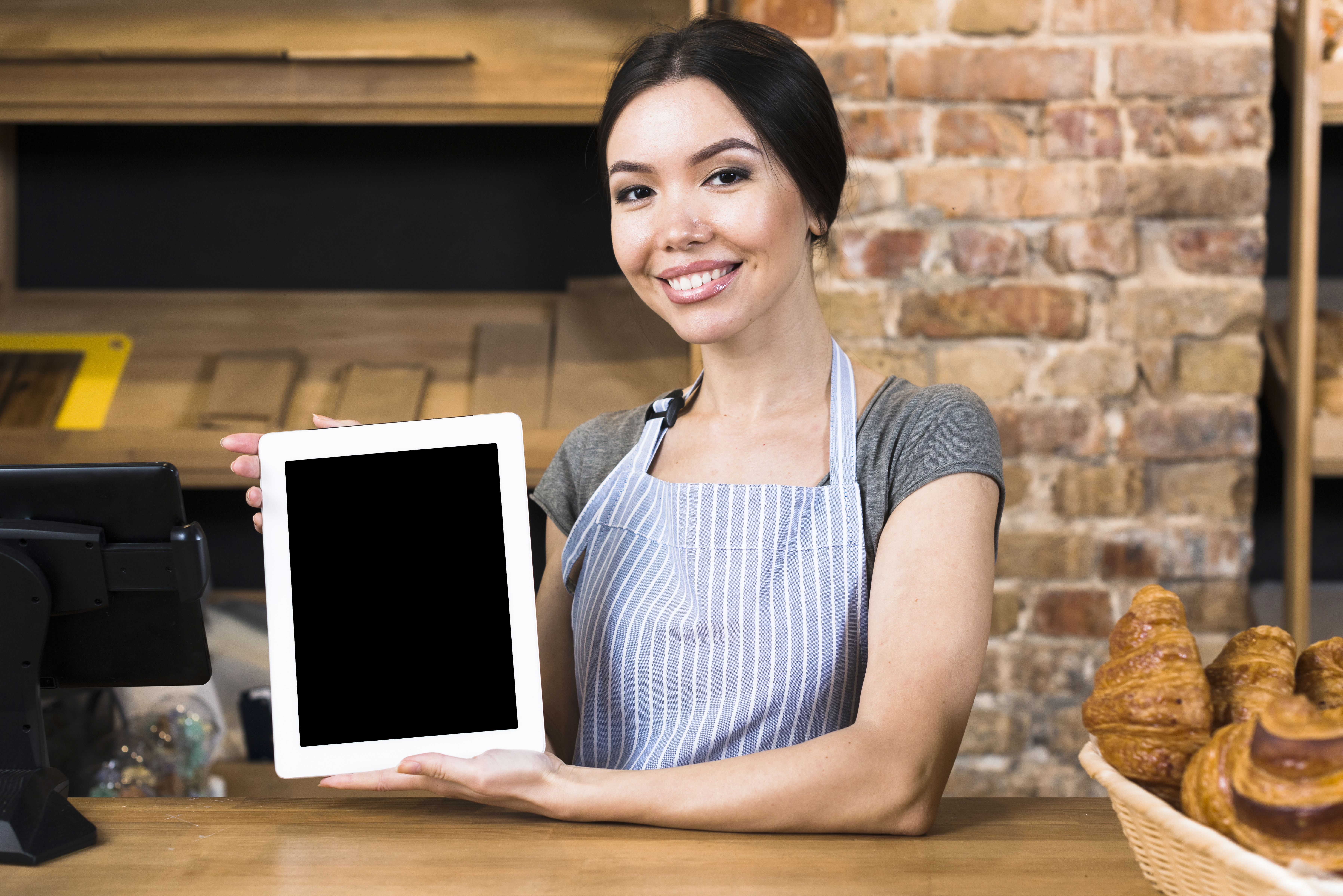 Woman wearing an apron, smiling, holding up an ipad in her hands with the screen showing.